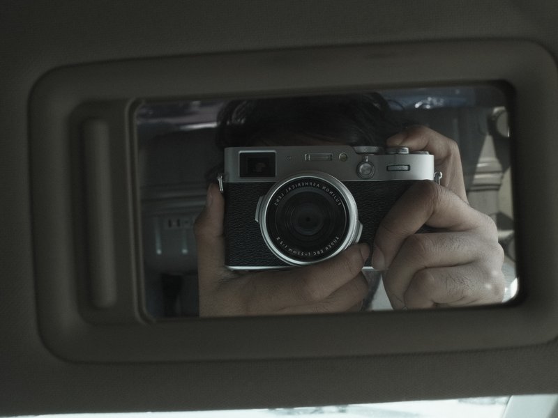 A reflection of a person holding a camera in a car's rearview mirror.