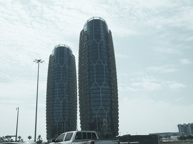 Two modern high-rise buildings with a unique design under a cloudy sky.