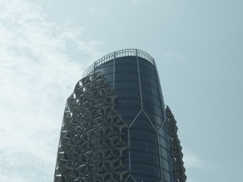 A modern skyscraper with intricate patterns on its facade against a pale blue sky.