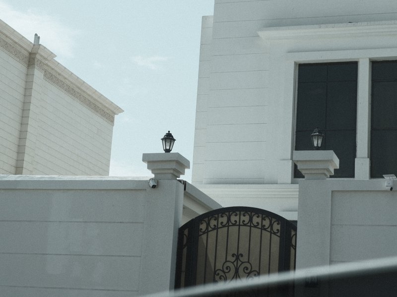 Close-up view of a white building's gate with decorative lamps on pillars.