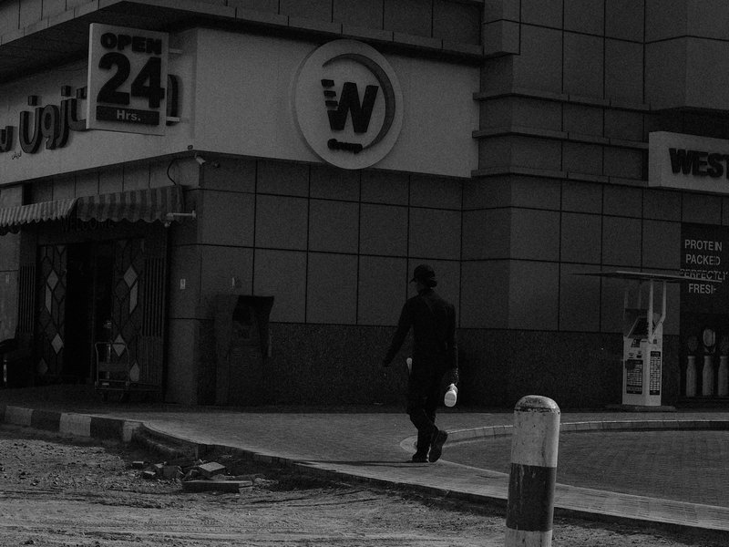 A solitary figure walking past a storefront in a dimly lit urban setting.