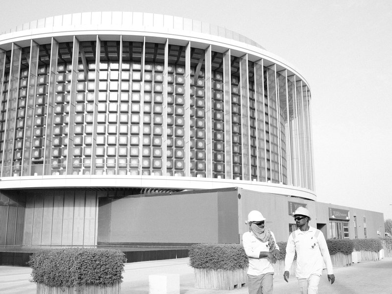 Two construction workers discussing in front of a modern building with a circular design.