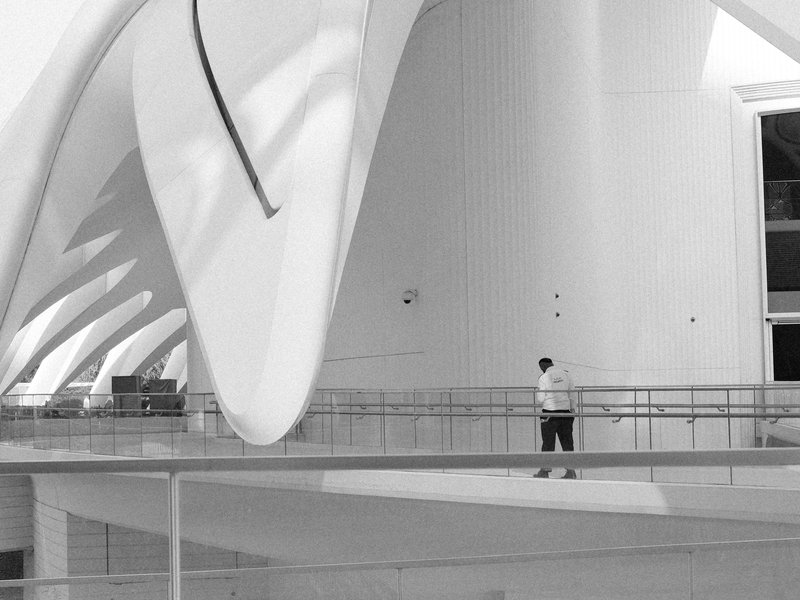 A lone figure stands in a modern architectural space with sweeping white curves and lines.