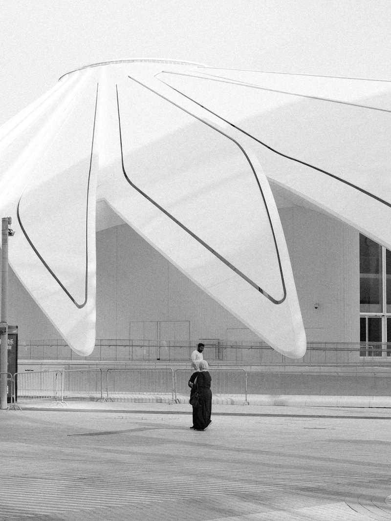 A person in traditional attire stands near a large, modern architectural structure with a petal-like design.