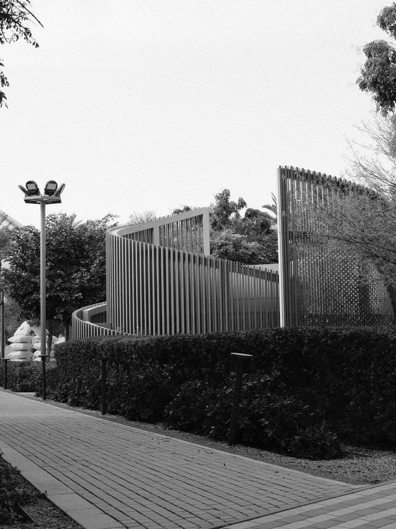 A modern architectural structure with curved lines surrounded by greenery and a pathway.