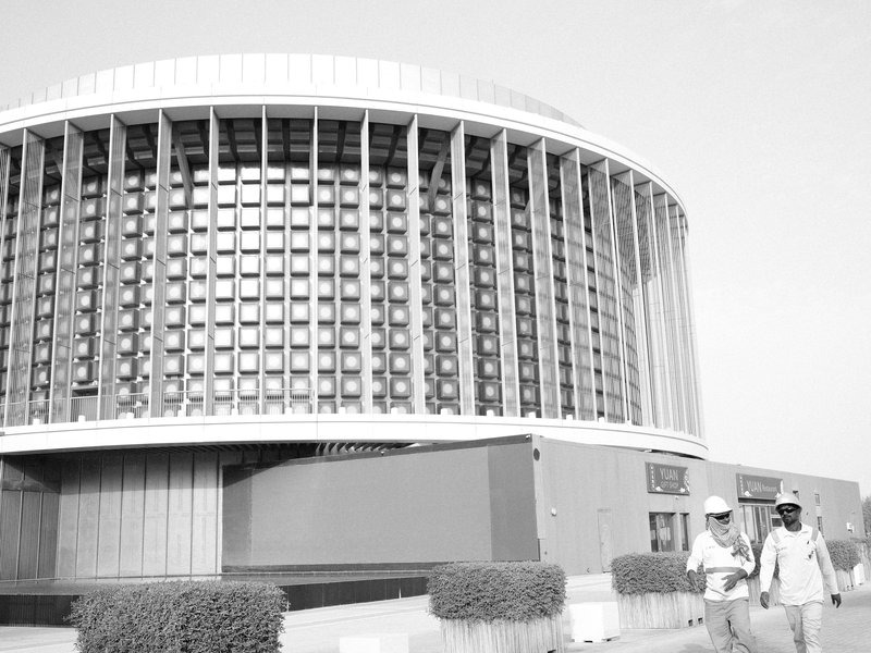Two people walking near a modern architectural building with circular design and large windows.