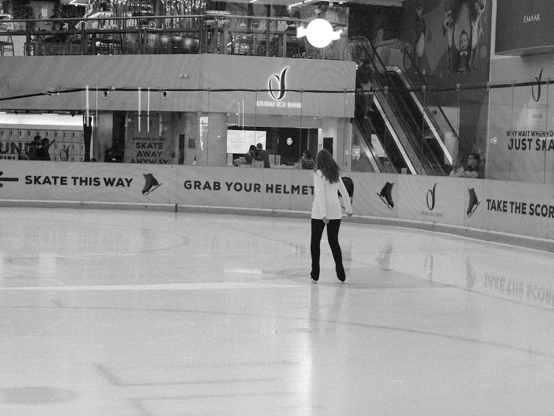 A solitary figure skating on an indoor ice rink with banners in the background.