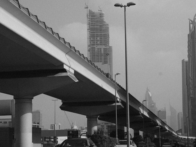 Black and white photo of an urban highway with a tall building under construction in the background.