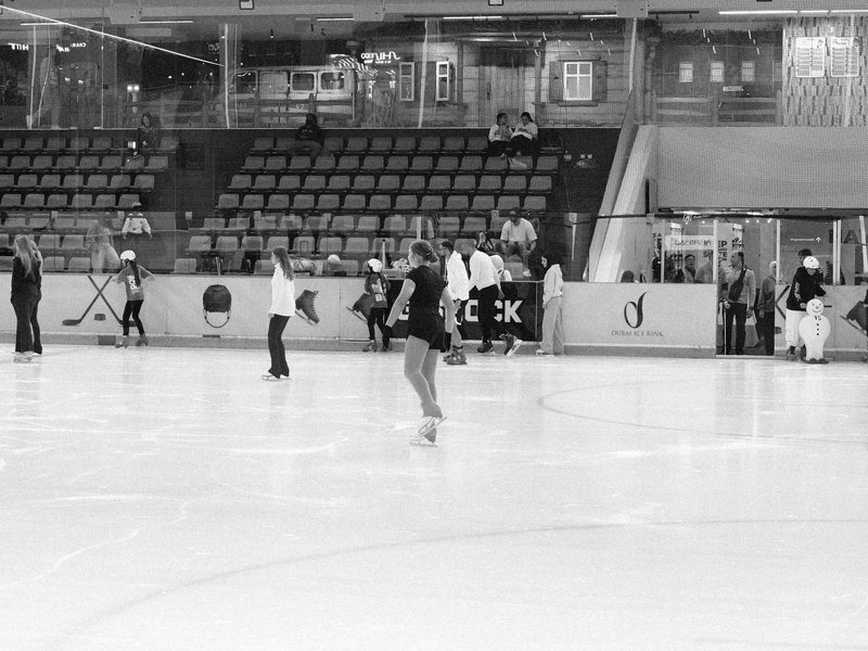 A figure skater practicing on an ice rink with spectators in the background.