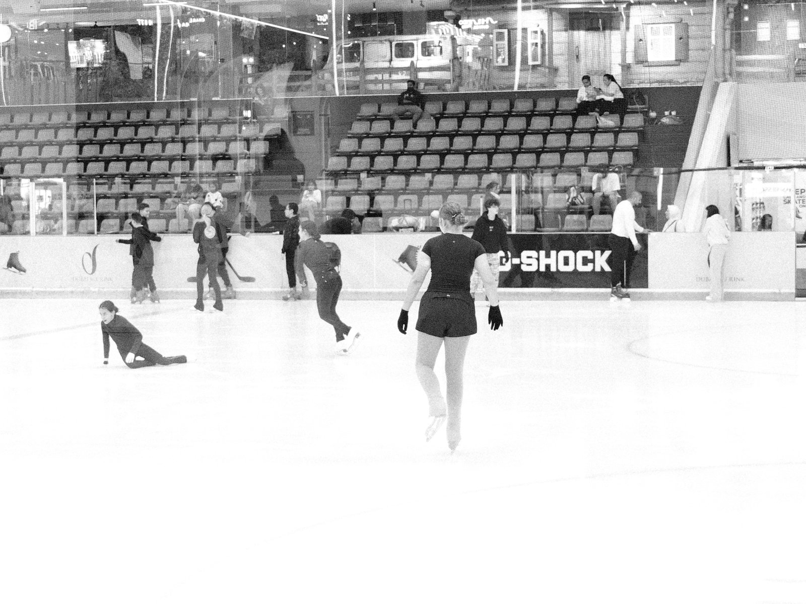 Figure skaters practicing on an ice rink with empty stands in the background.