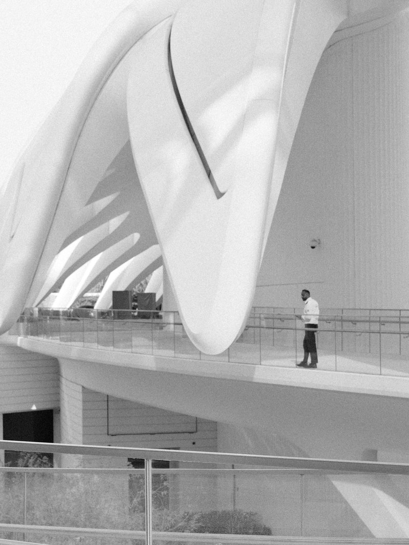 A person standing on a balcony of a modern architectural structure with large white curves.