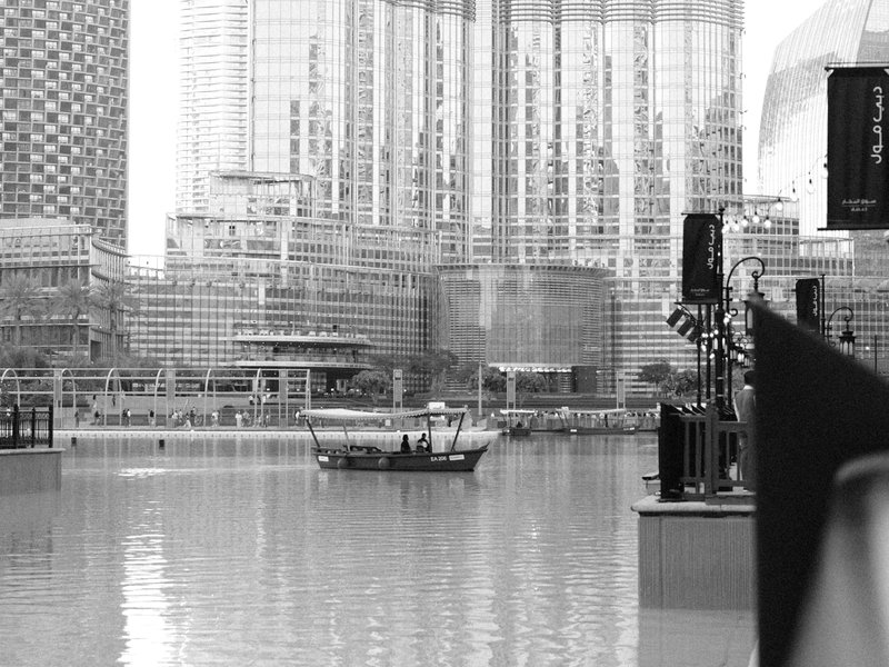 A boat on a calm water body with modern buildings reflecting in the background.