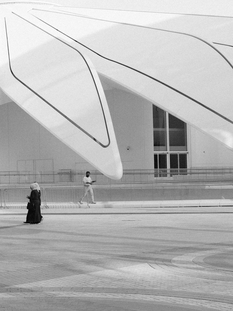 A woman in traditional attire walks past a modern architectural structure with large, curved features.