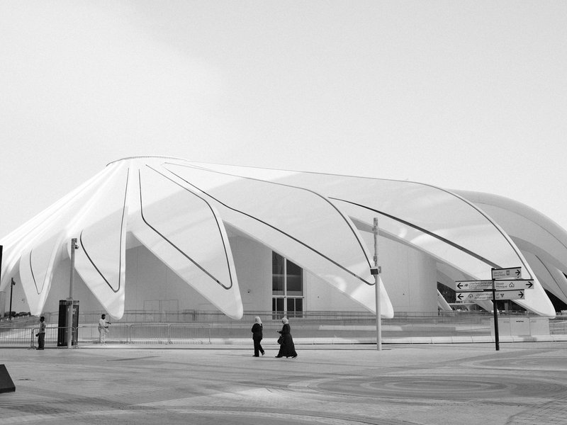Two people walking in front of a modern architectural building with a unique white design.