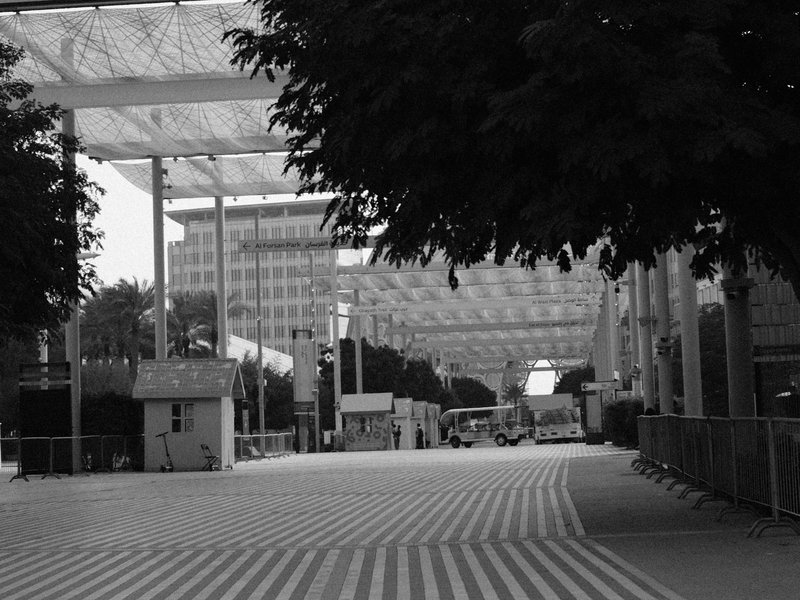 A deserted urban street with striped pavement and modern architecture under a cloudy sky.