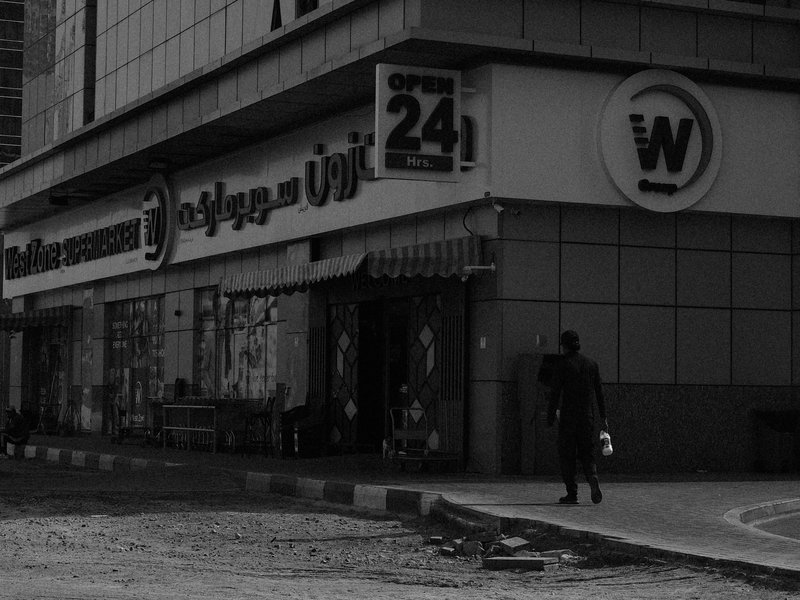 A person walking past a storefront in a city, with a focus on the building's signage and urban environment.