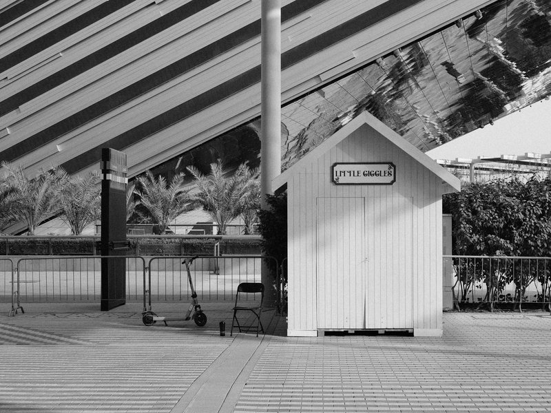 A small white shed with a sign, set against a backdrop of striped architecture and palm trees.