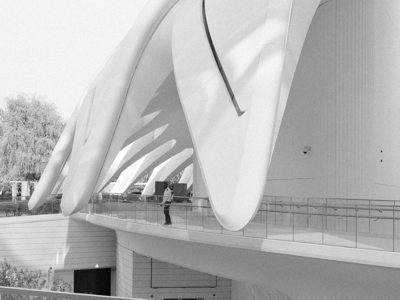 A person standing on a balcony of a modern architectural structure with flowing white forms.