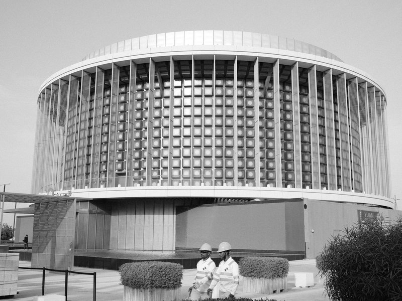 A modern circular building with large windows and two people sitting in front.