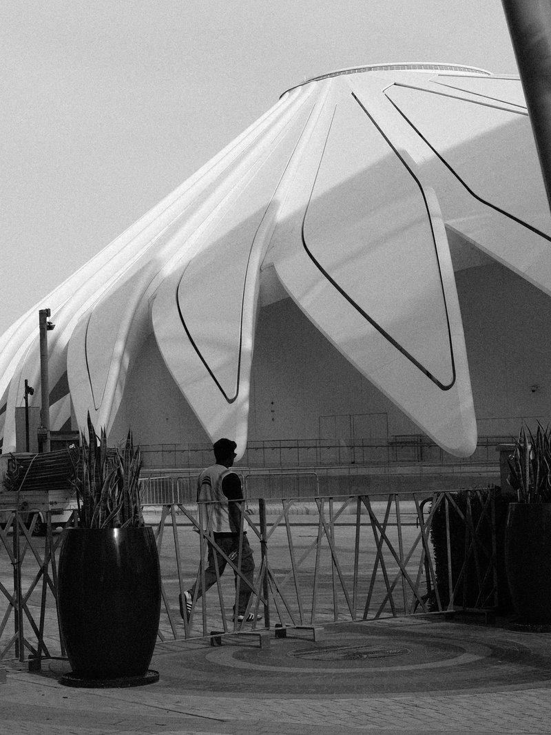 A person walking near a modern architectural structure with a unique, curved roof design.