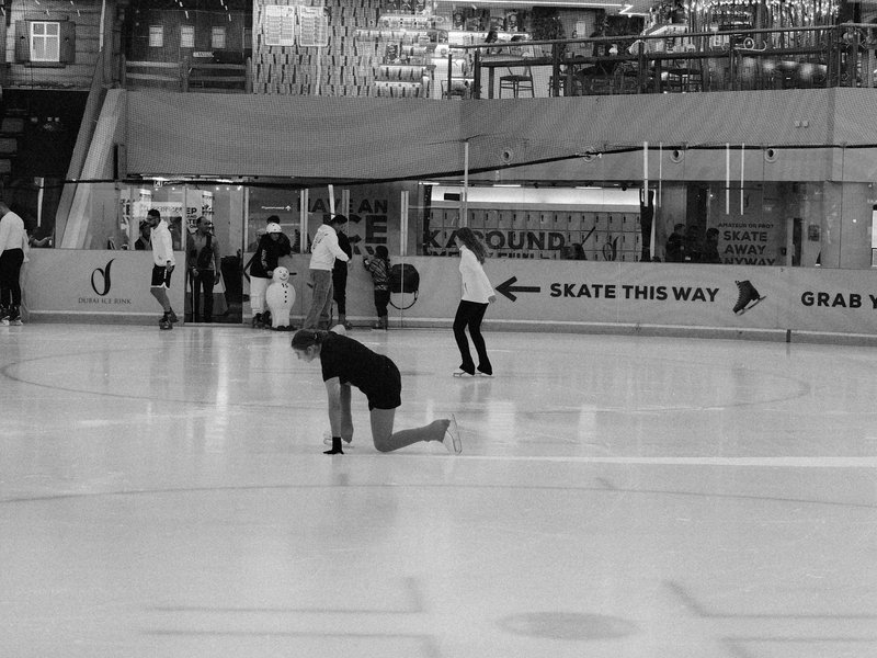 A black and white image of skaters on an ice rink, with a focus on one skater in a black outfit.