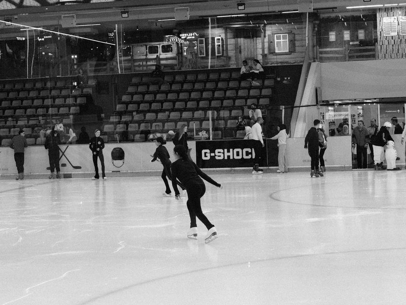 A black and white image of skaters practicing on an ice rink in a sports arena.