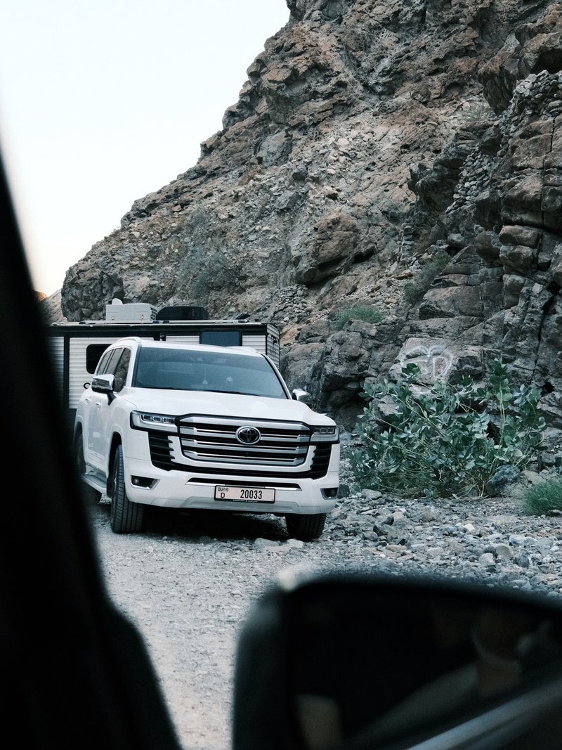 A white SUV parked on a rocky road with mountains in the background.
