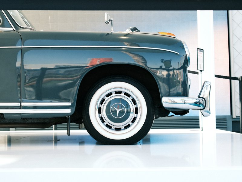 Side view of a classic car showcasing its wheel and chrome details against a light background.