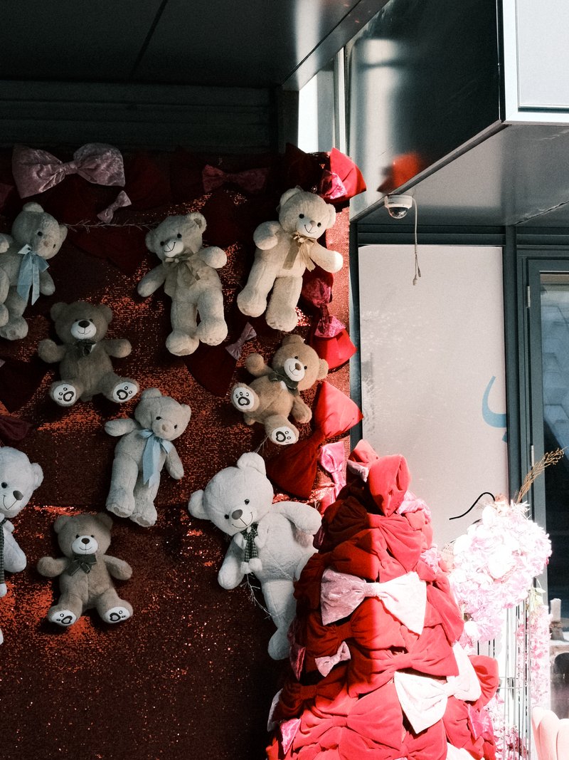 A display of teddy bears on a red backdrop with decorative bows and a soft, warm atmosphere.