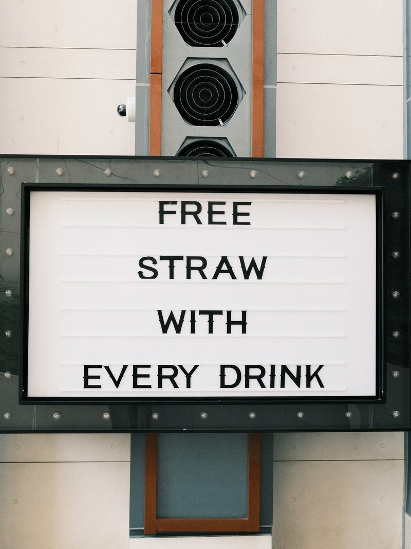 Signboard displaying 'Free Straw With Every Drink' in bold letters against a decorative background.