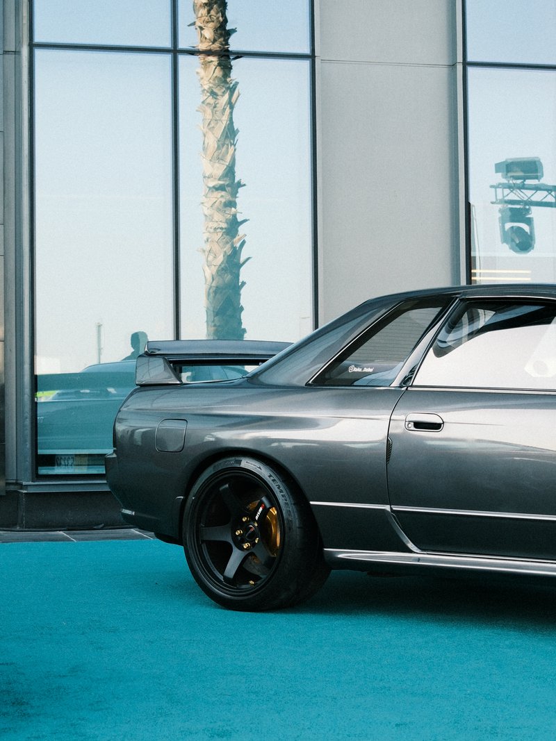 A sleek gray sports car parked beside a glass building with palm trees in the background.