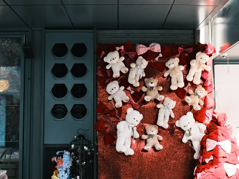 A display of teddy bears on a red backdrop with decorative elements and hats in the background.