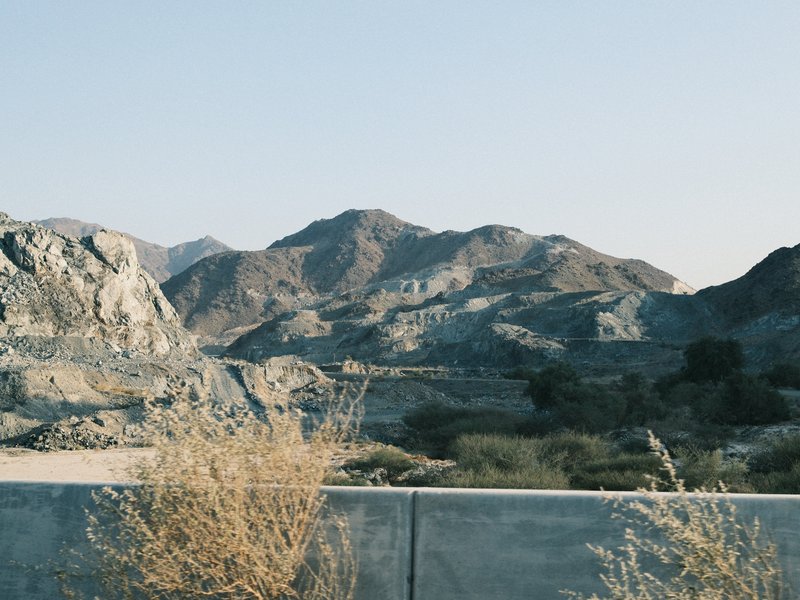 A rocky mountain landscape with dry vegetation in the foreground under a clear sky.
