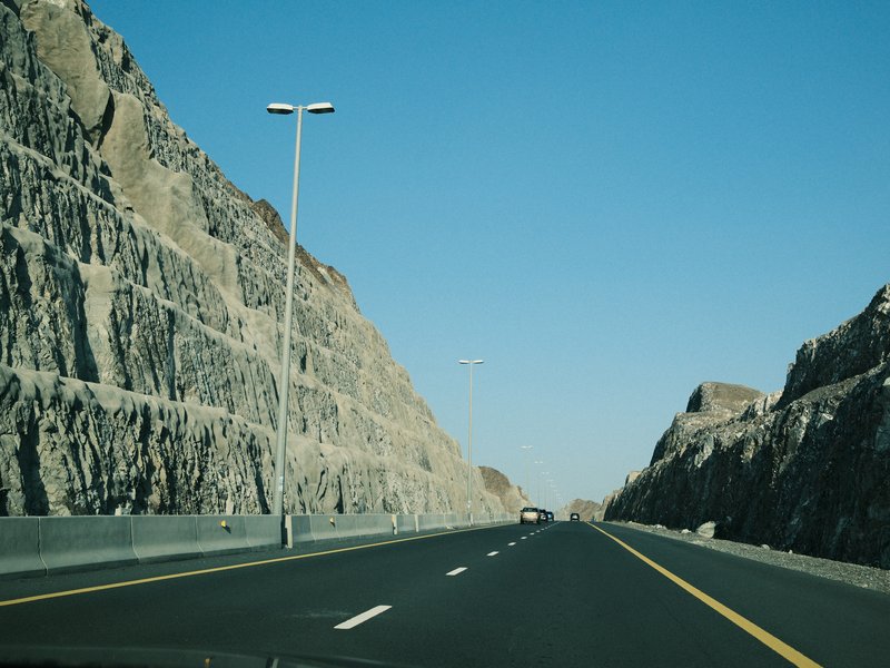 A highway flanked by rocky cliffs under a clear blue sky.