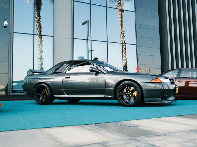 A sleek gray sports car parked on a turquoise surface in front of a modern glass building.