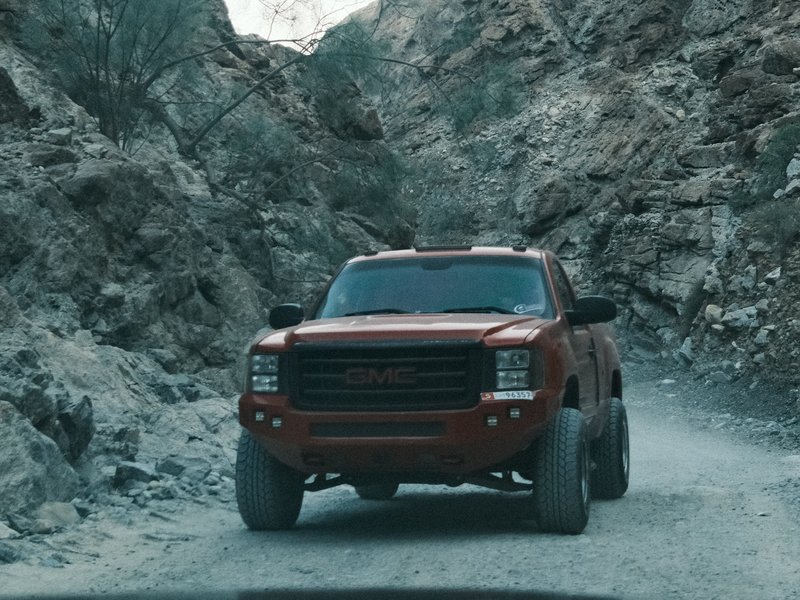 A red truck driving on a rocky mountain road surrounded by steep cliffs.