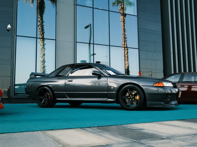 A sleek gray sports car parked on a turquoise surface with palm trees and a modern building in the background.