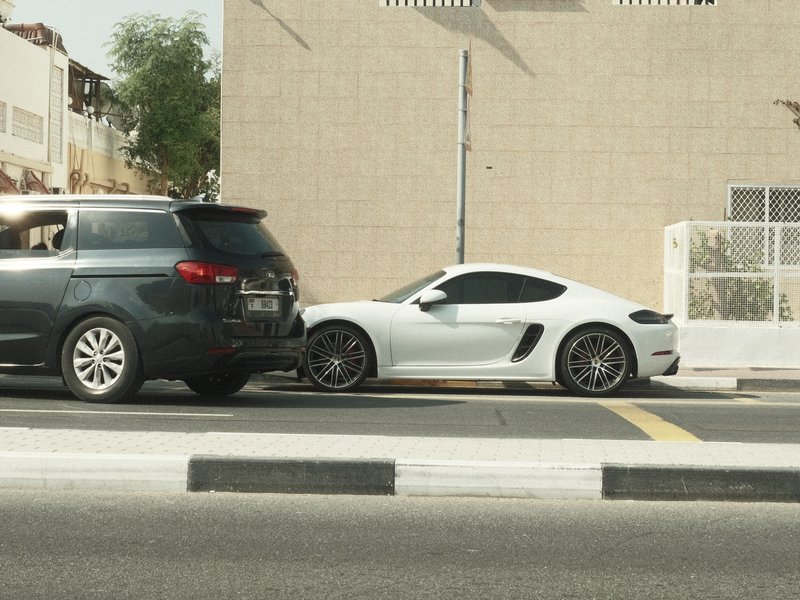 A black SUV parked beside a white sports car on a city street with buildings in the background.