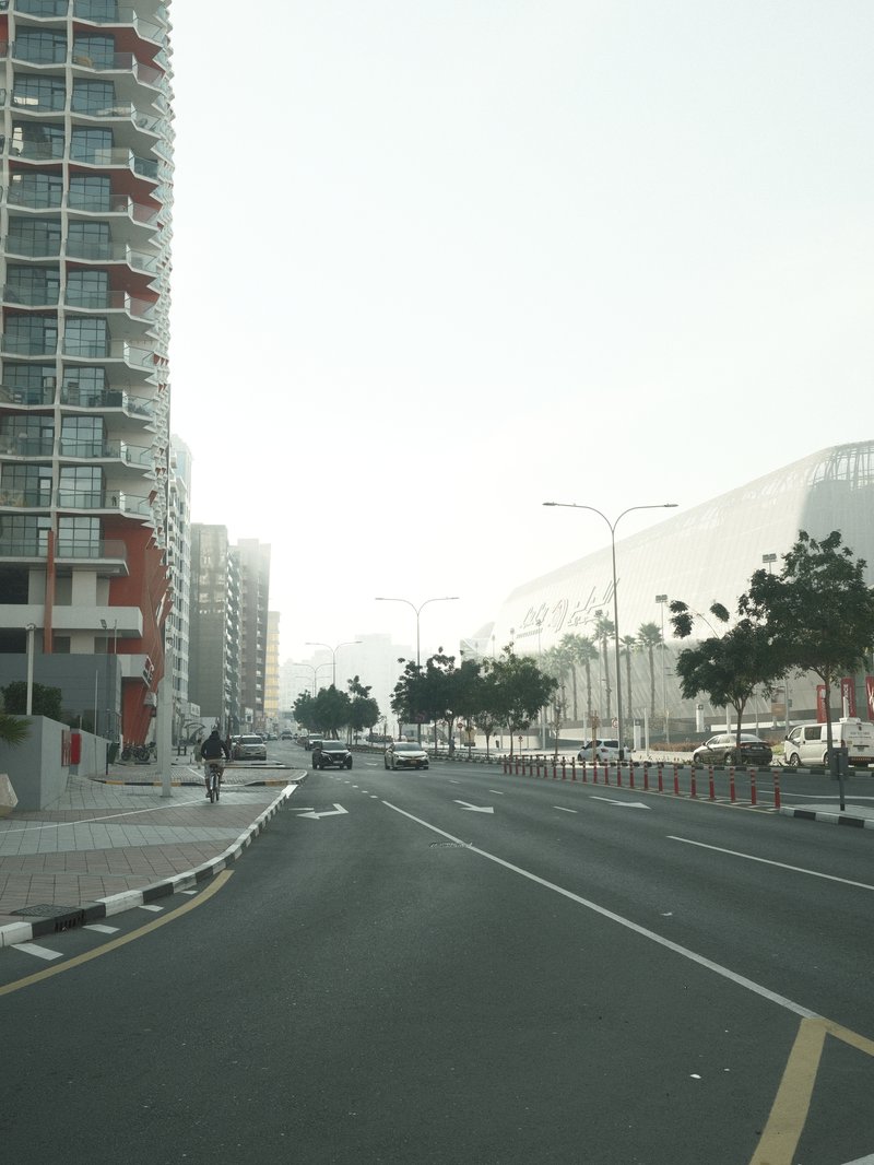 A quiet urban street with tall buildings on either side, shrouded in soft morning light.