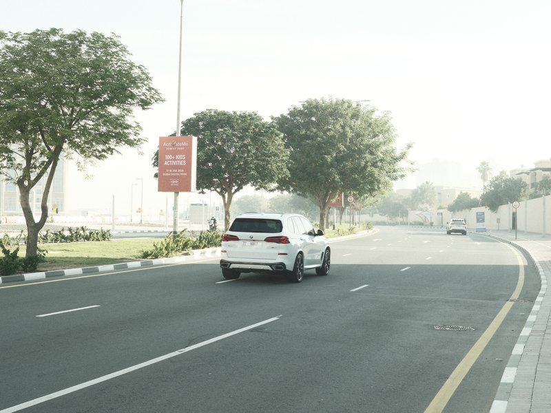 A white SUV driving on a quiet road lined with trees in a hazy atmosphere.
