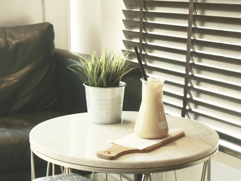 A cozy indoor scene featuring a drink on a marble table beside a potted plant and a leather couch.