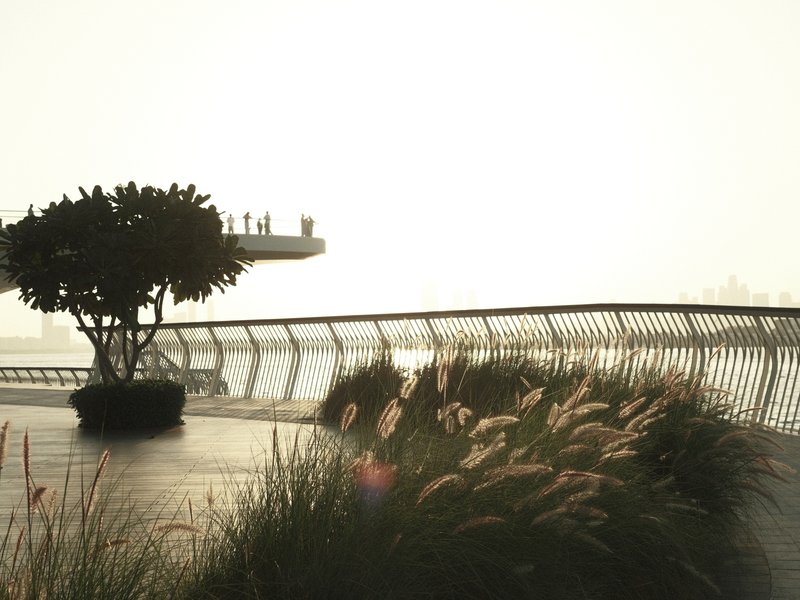 A serene waterfront scene with tall grasses and a tree, overlooking a distant platform in bright light.