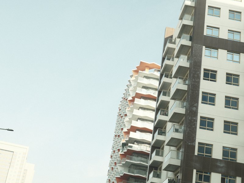 Two modern apartment buildings against a clear sky, showcasing architectural design and urban living.