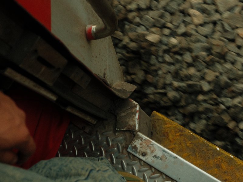 Close-up of a person's hand on a metal step of a train, with gravel visible below.