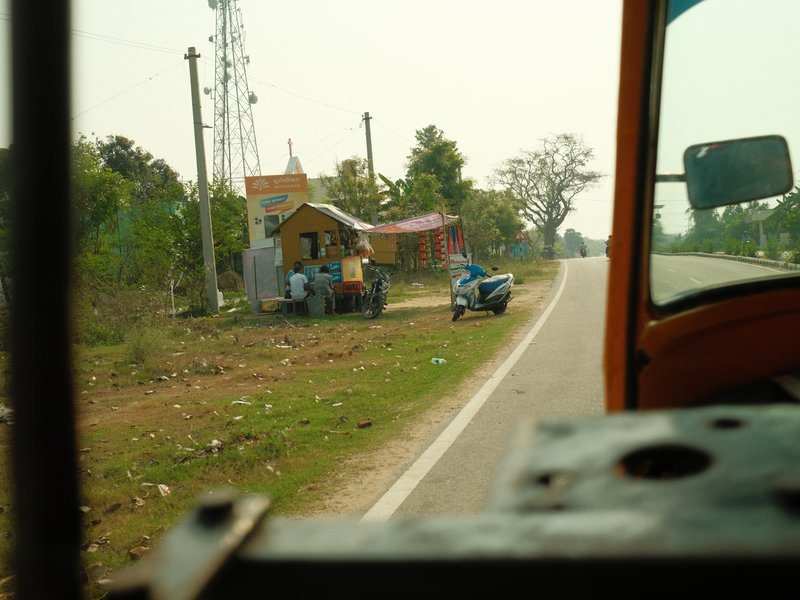 View from a vehicle showing a rural roadside with a small structure and a motorcycle parked nearby.