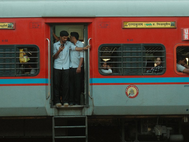 Two young men standing at the entrance of a red train, with passengers visible inside.