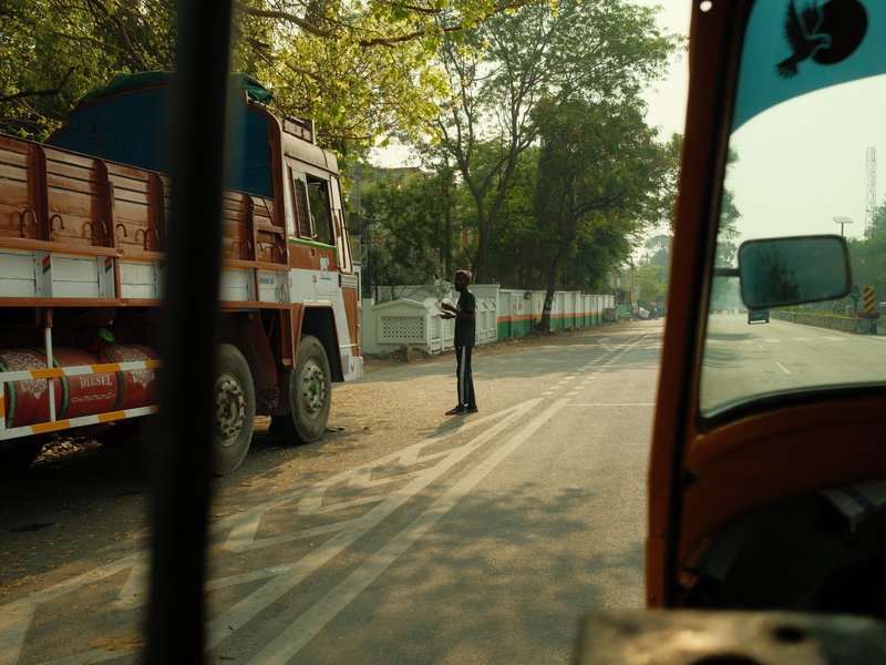 A street scene featuring a truck and a person standing by the roadside, captured from an auto rickshaw.
