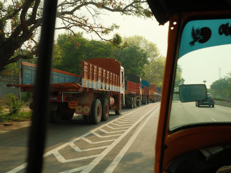 View from a vehicle showing a line of trucks on a road with trees in the background.