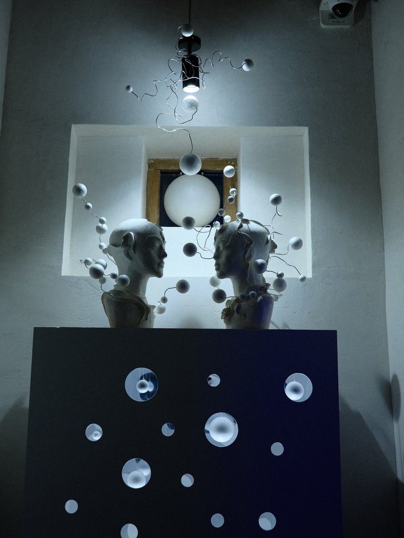 Two white sculptures of heads facing each other, surrounded by floating spheres and soft lighting.