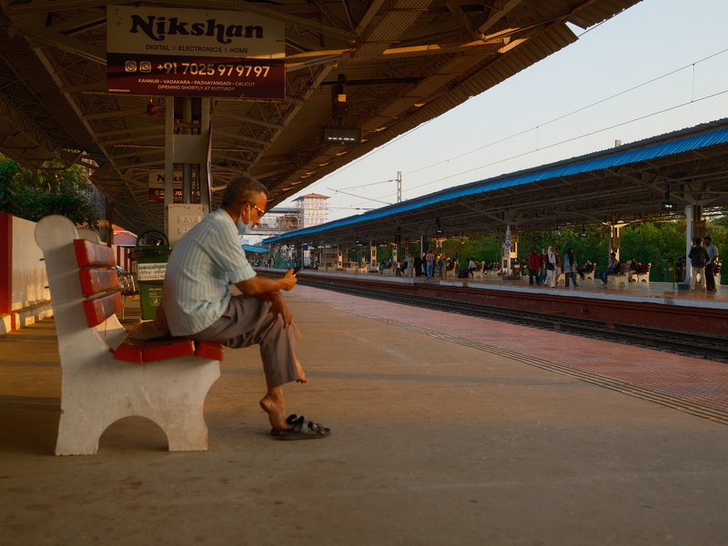 An elderly man sitting on a bench at a train station, waiting for a train during golden hour.